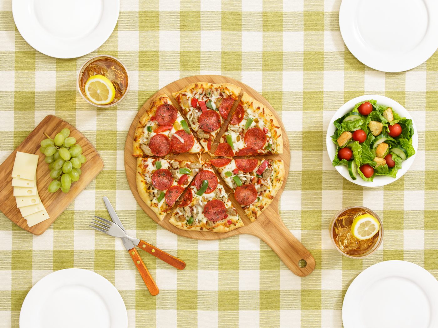 Overhead commercial food photograph of pizza, salad, drinks, and table settings on a checked cloth