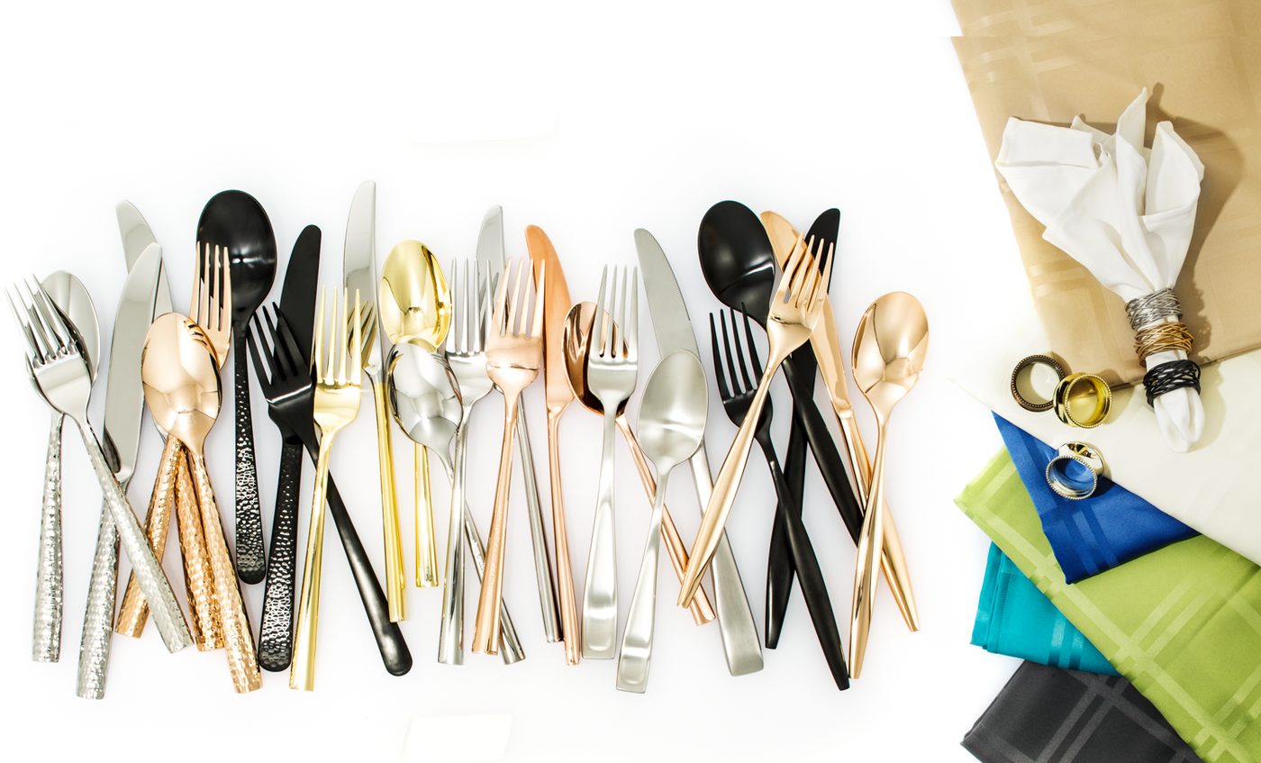 Overhead product arrangement of mixed-metal flatware, napkins, and rings on a white surface
