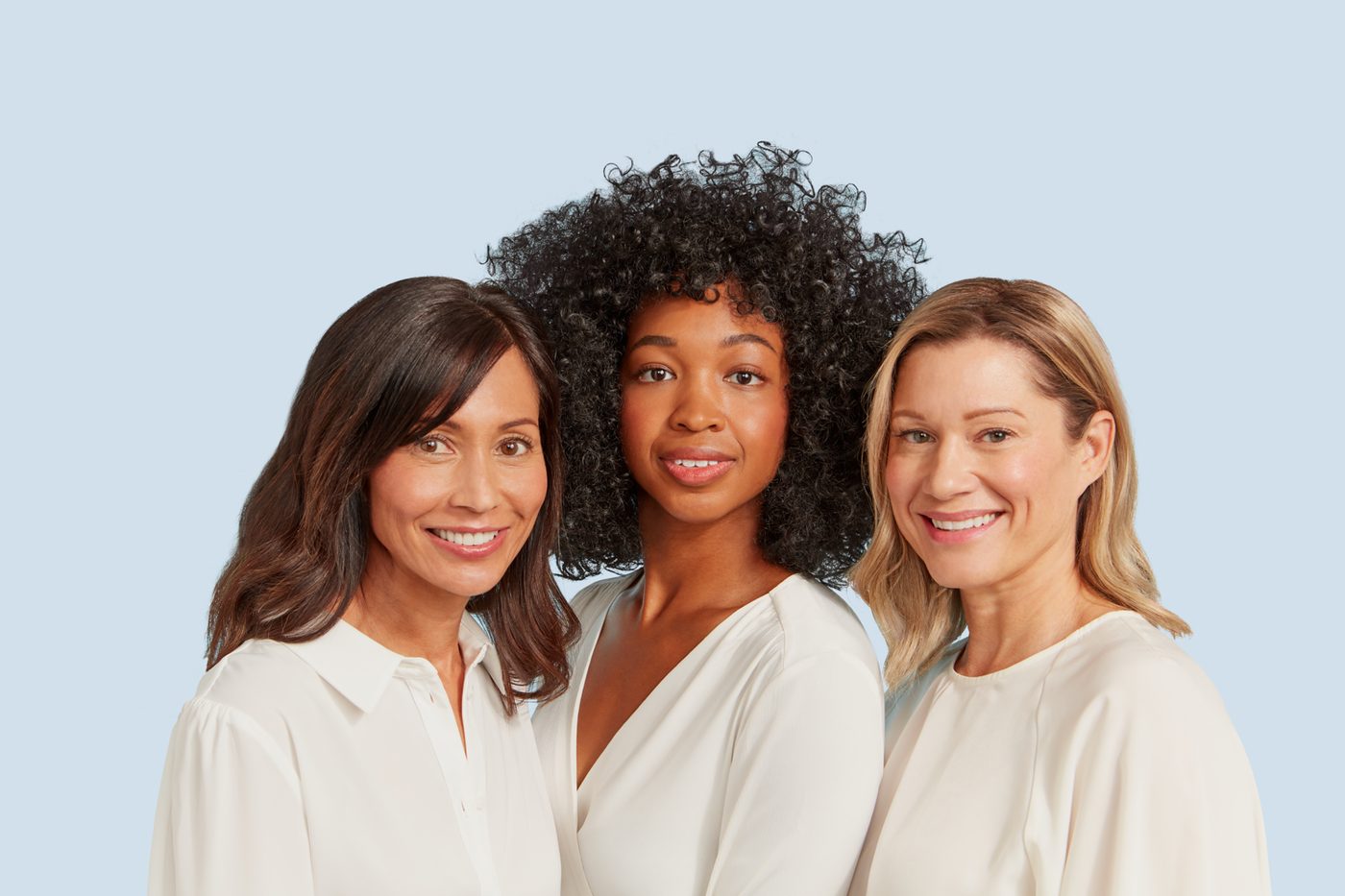 Commercial group portrait of three women wearing light clothing against a pale blue background