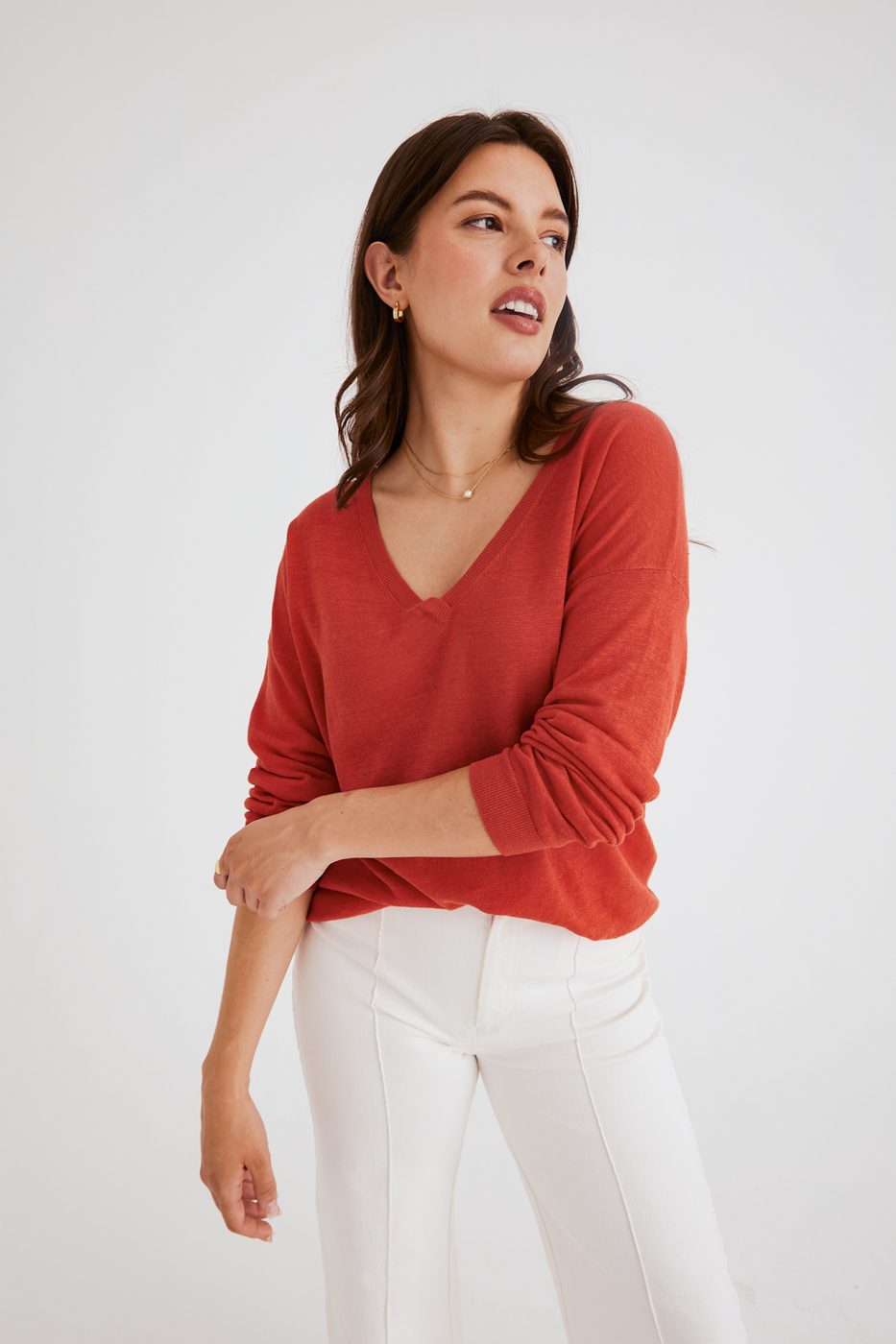 Ecommerce apparel image of a woman wearing a paprika-red knit top and white pants against a light gray background